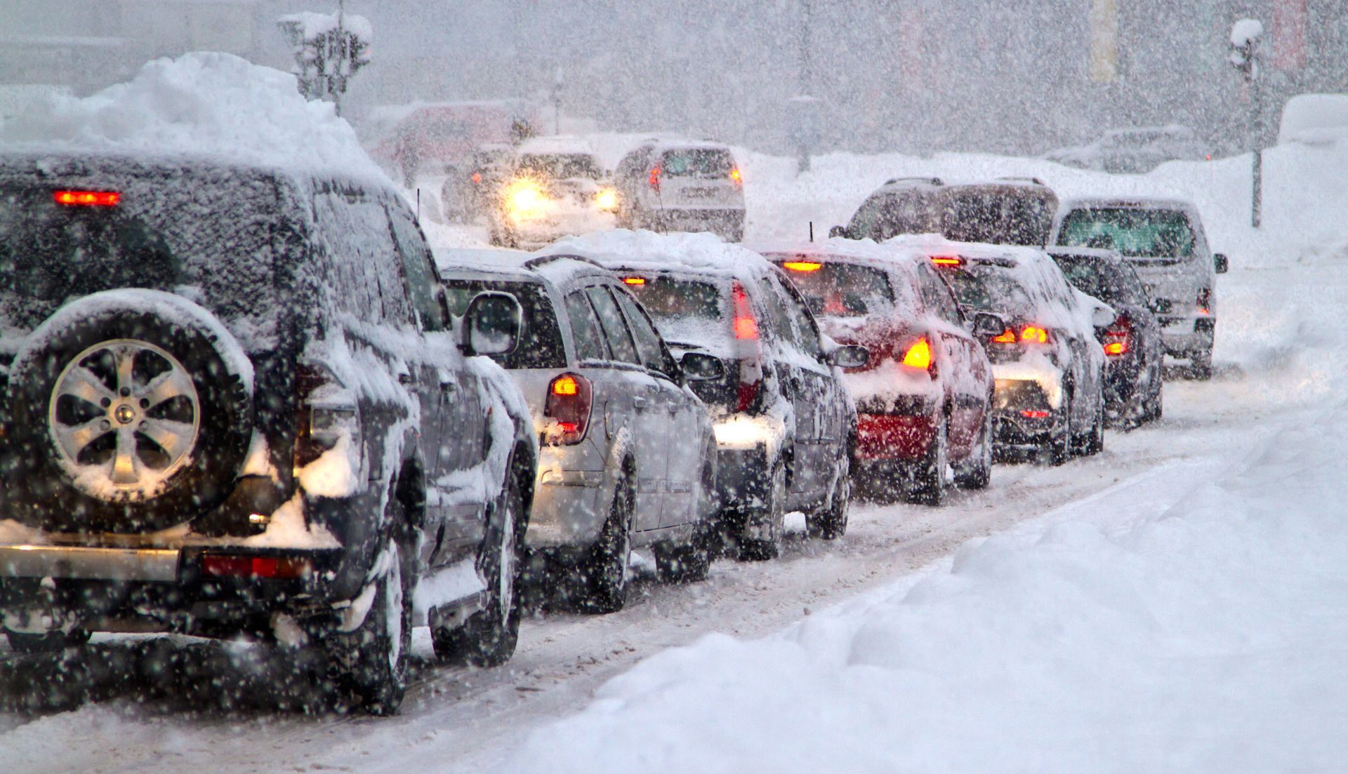 Cars wait in heavy traffic on a snow-covered city street during a winter snowstorm.