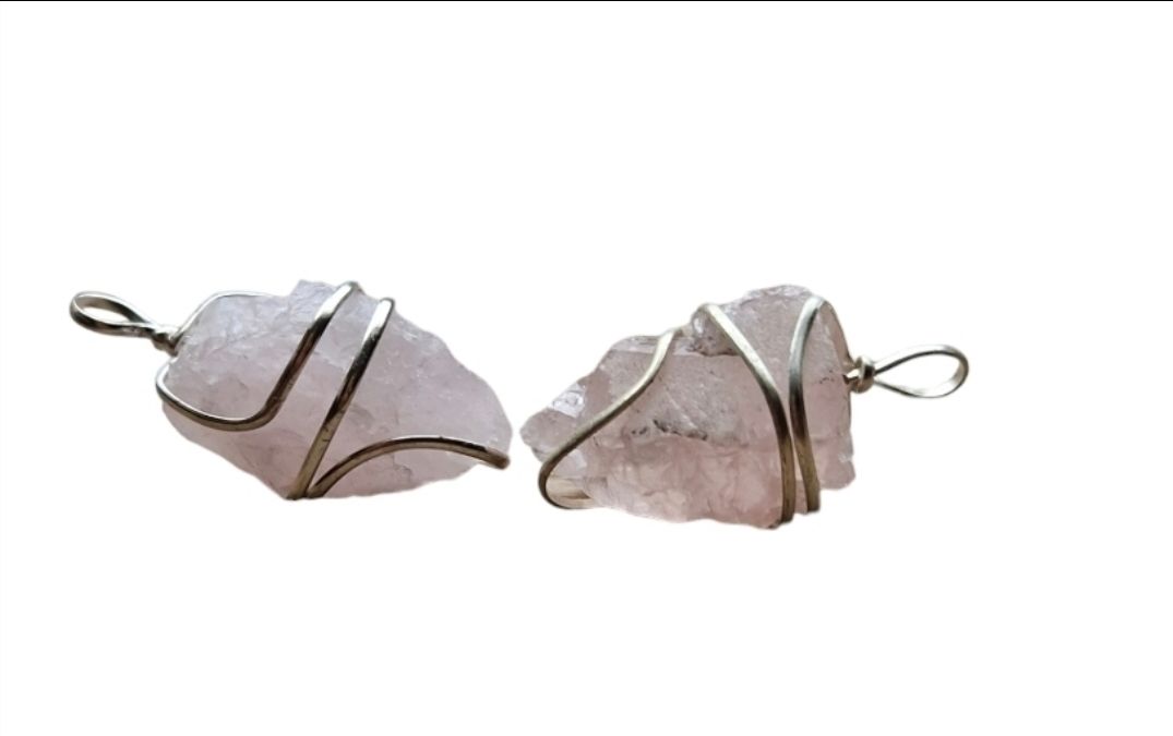 Twee hangers van rozenkwarts, omwikkeld met zilverkleurig draad, geïsoleerd op een witte achtergrond.