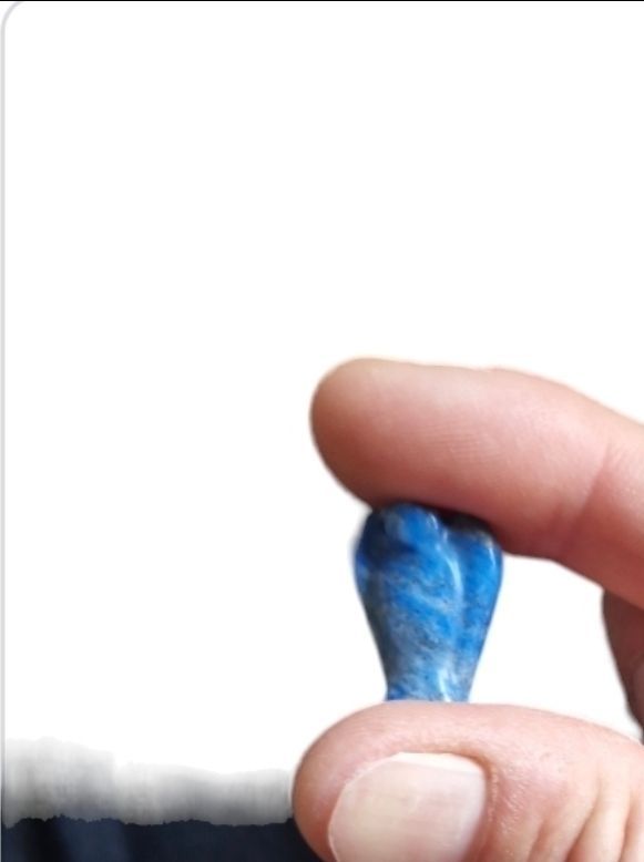Een hand die een klein, blauw, hartvormig steentje vasthoudt tegen een witte achtergrond.