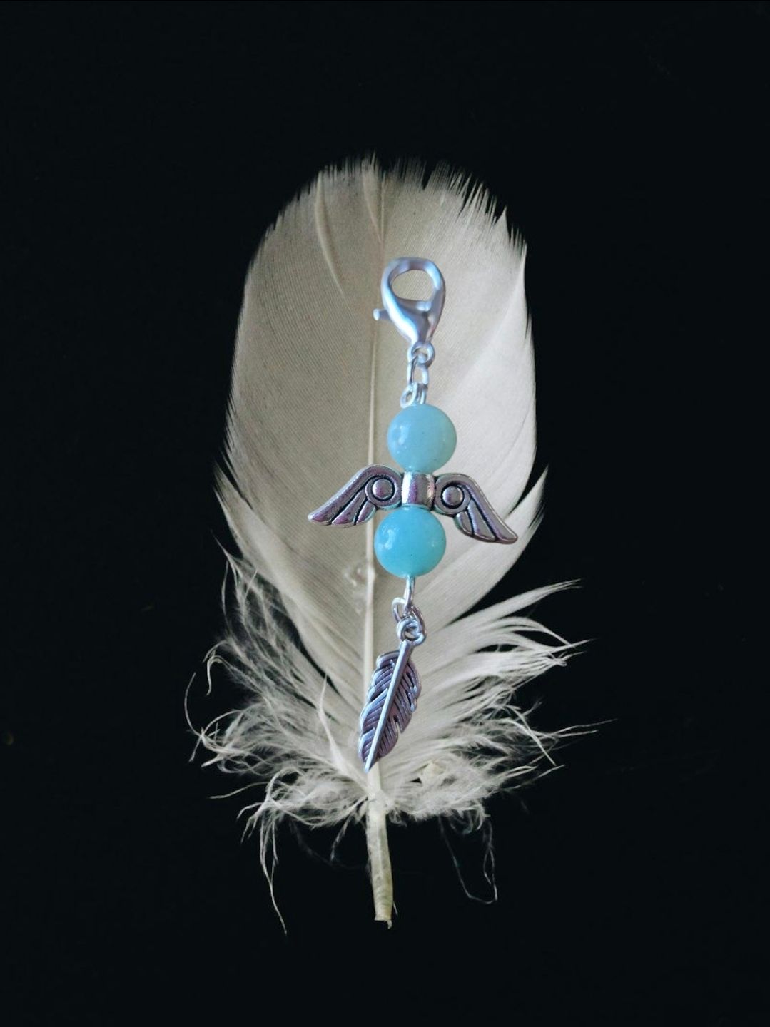 Witte veer met een bedeltje bestaande uit blauwe kralen, zilveren vleugels en een veer.