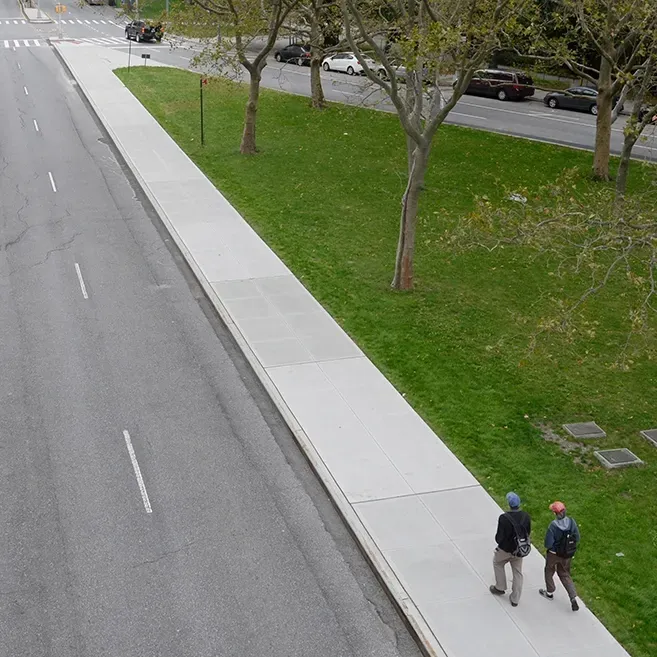 Two people walking down a sidewalk next to a road