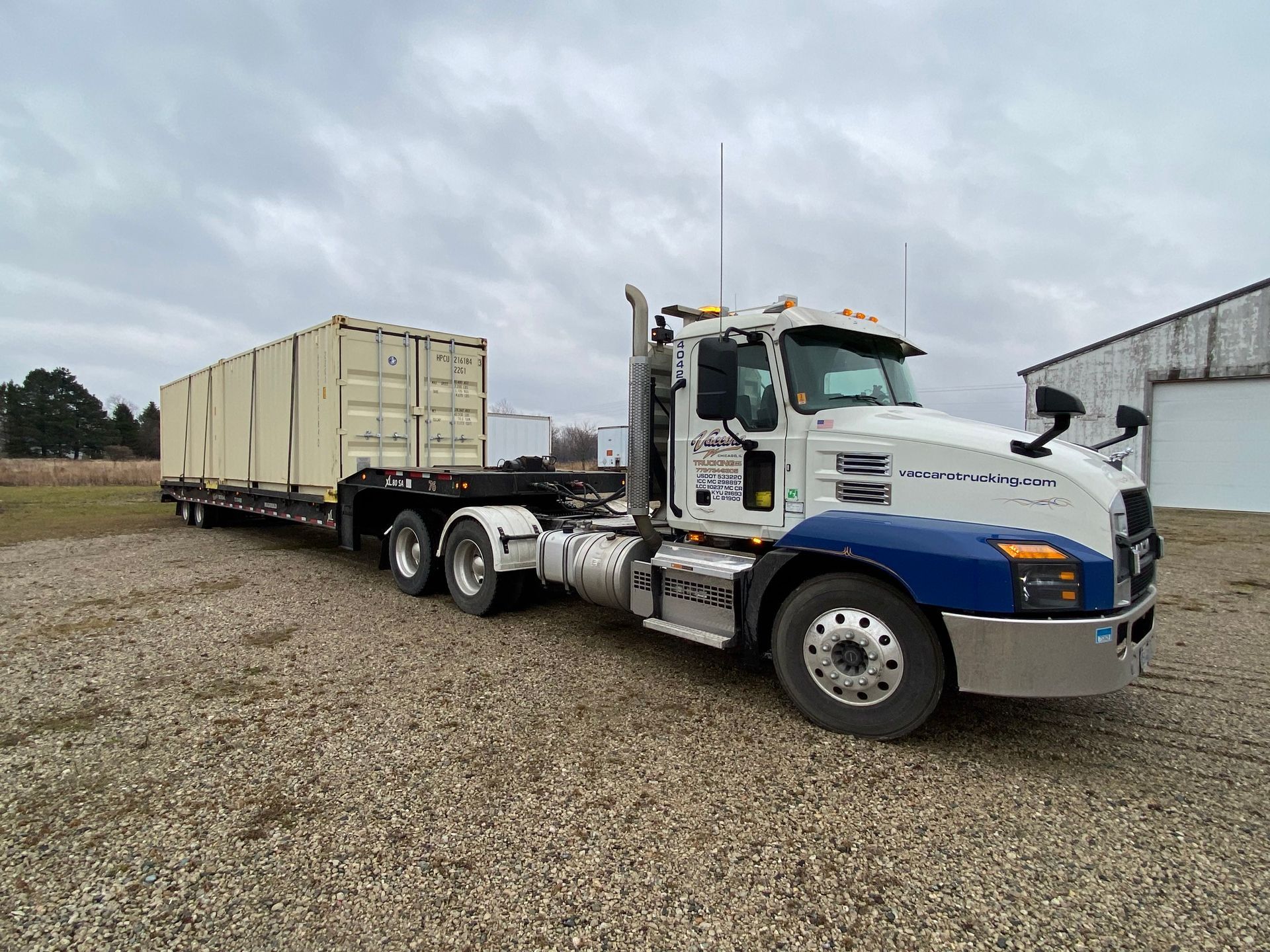 A semi truck with a trailer attached to it is parked in a gravel lot.