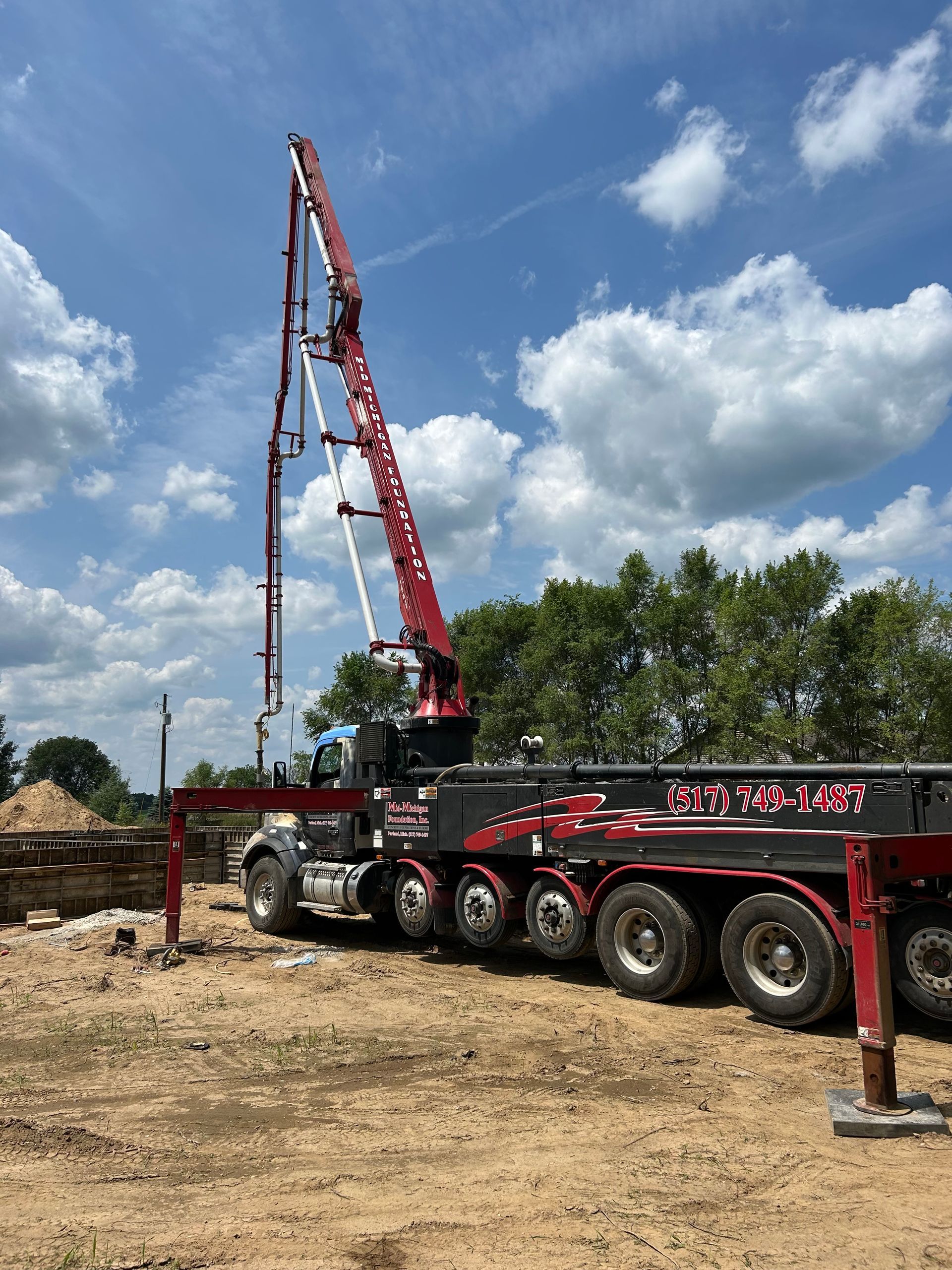 A red and black truck with a crane attached to it is parked in a dirt field.