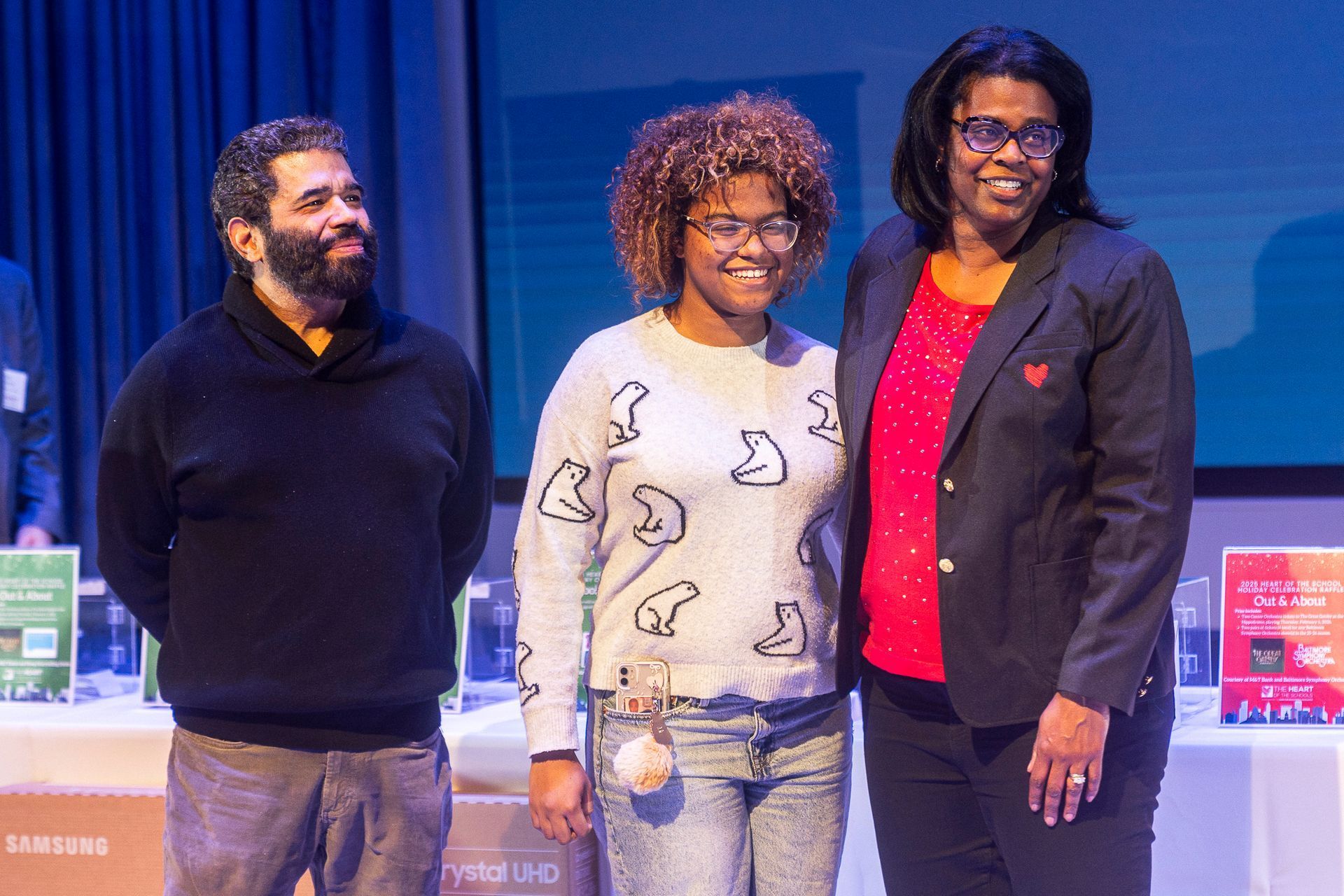 HOS Holiday Celebration - Three people on a stage with awards. Man with beard, woman in sweater, woman in blazer, smiling.