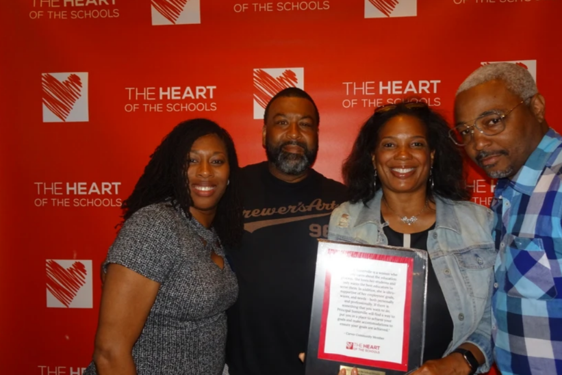 HOS Honors - Four people holding an award in front of a red backdrop with