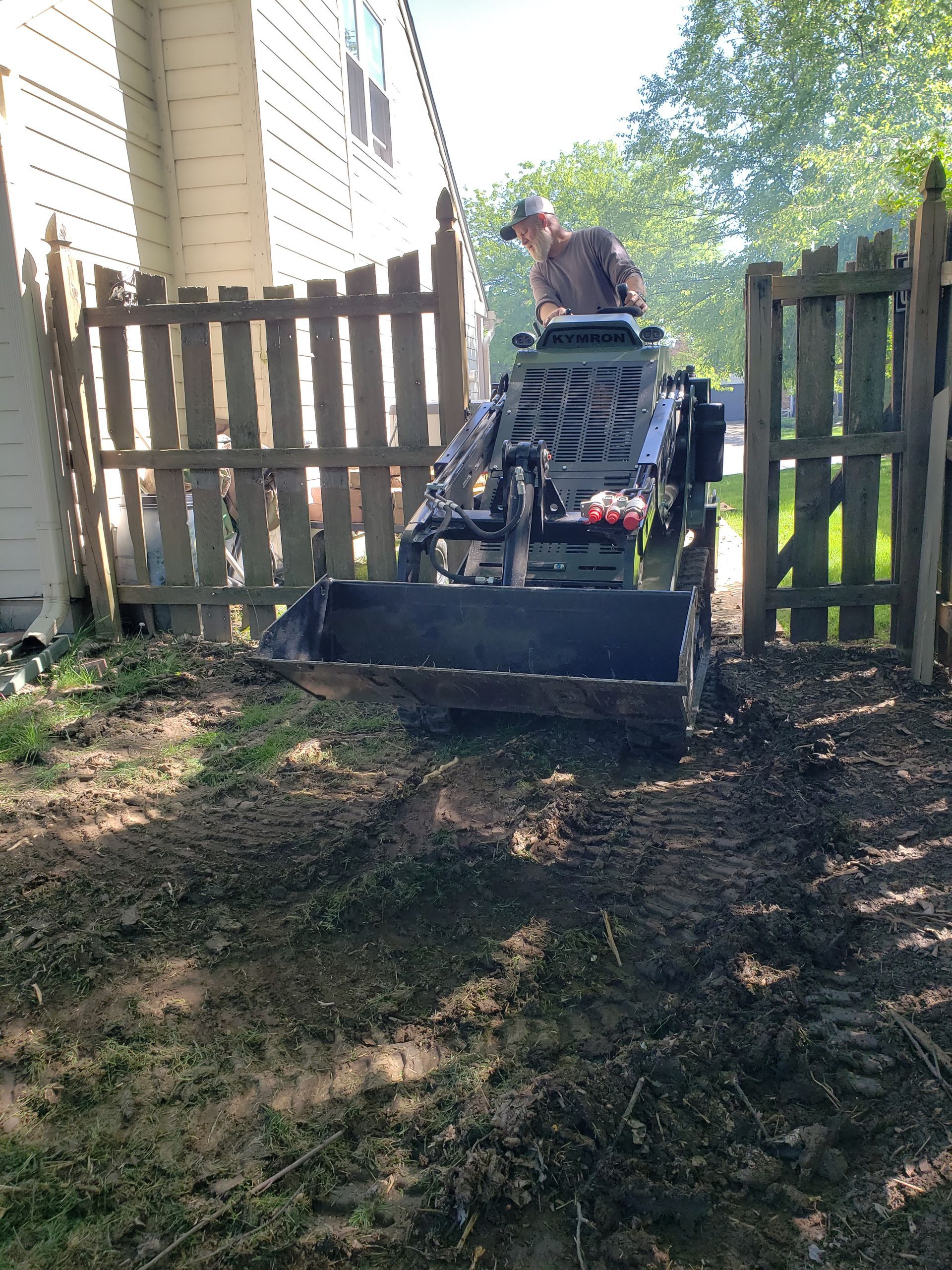 A man is driving a tractor in a backyard next to a wooden fence.