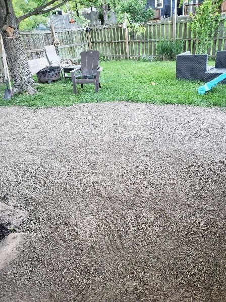A gravel patio with chairs and a fire pit in a backyard. A gravel patio with chairs and a fire pit in a backyard.