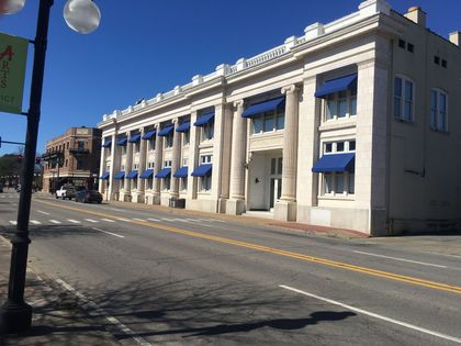 Exterior of a brick building under construction with grey siding, metal awnings over doors, and a blue handicap sign.