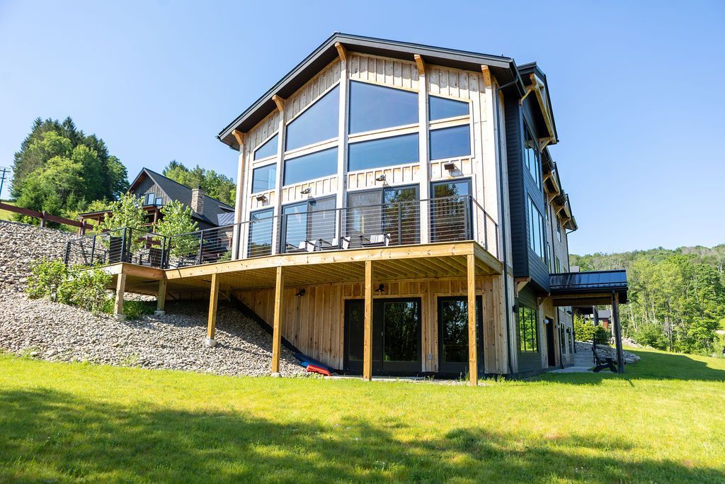 New Build Home in Ellicottville NY. Image of a new modern house with large windows on a grassy hillside under a clear blue sky