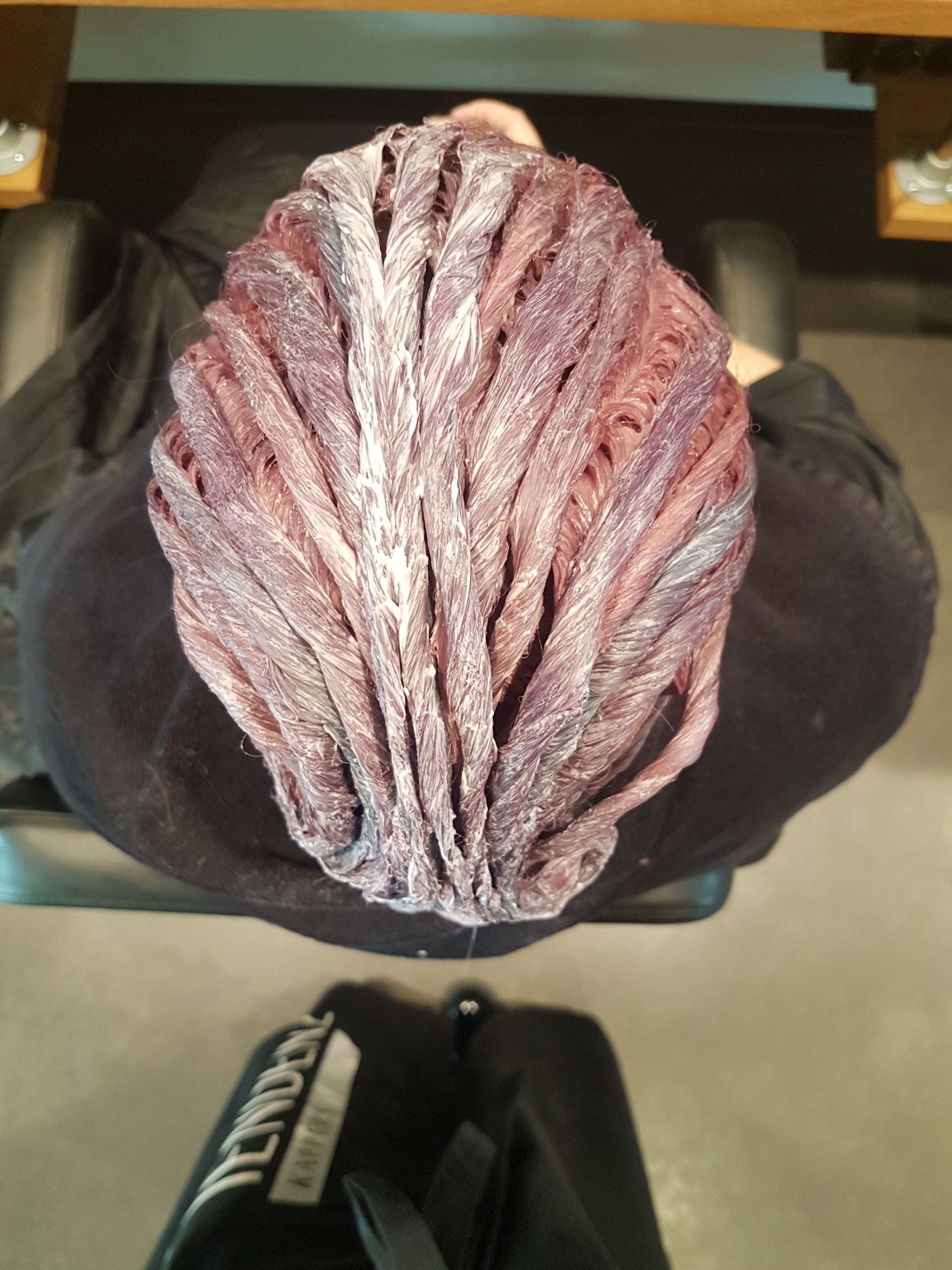Bovenaanzicht van een persoon met roze gevlochten haar, zittend tegen een donkere achtergrond.