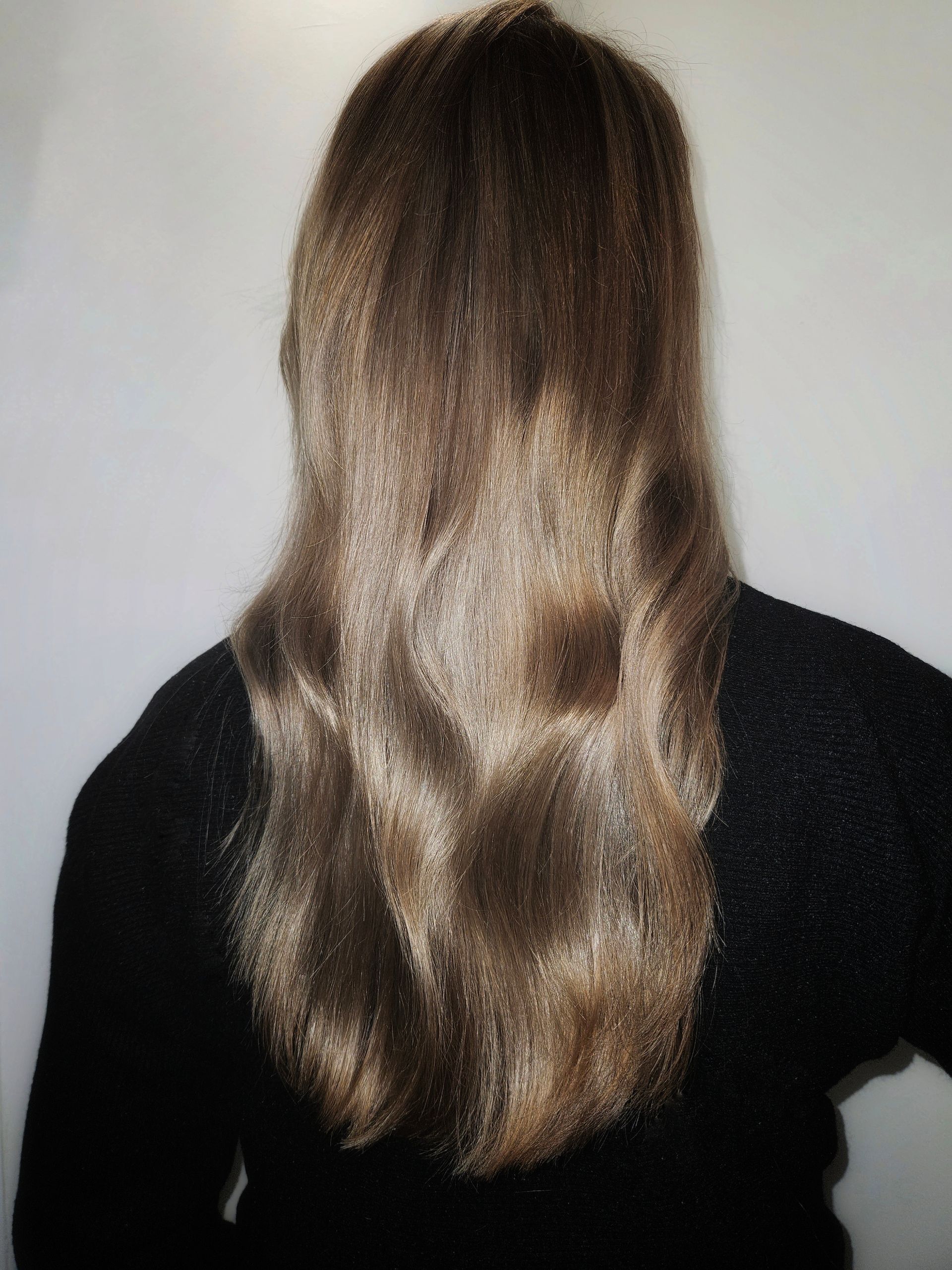 Achteraanzicht van een persoon met lang bruin haar, gekleed in een zwart shirt, tegen een effen achtergrond.