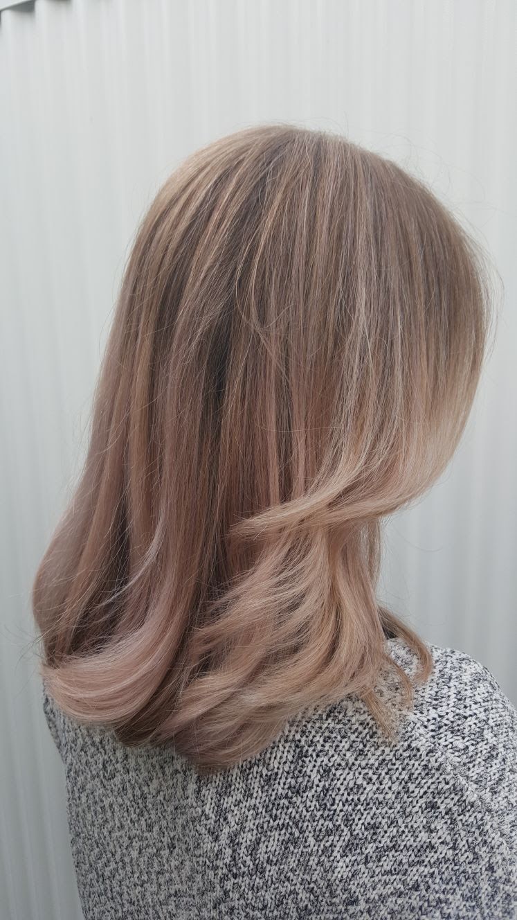 Schouderlang, golvend bruin haar met blonde highlights, van achteren gezien tegen een licht gestreepte achtergrond.