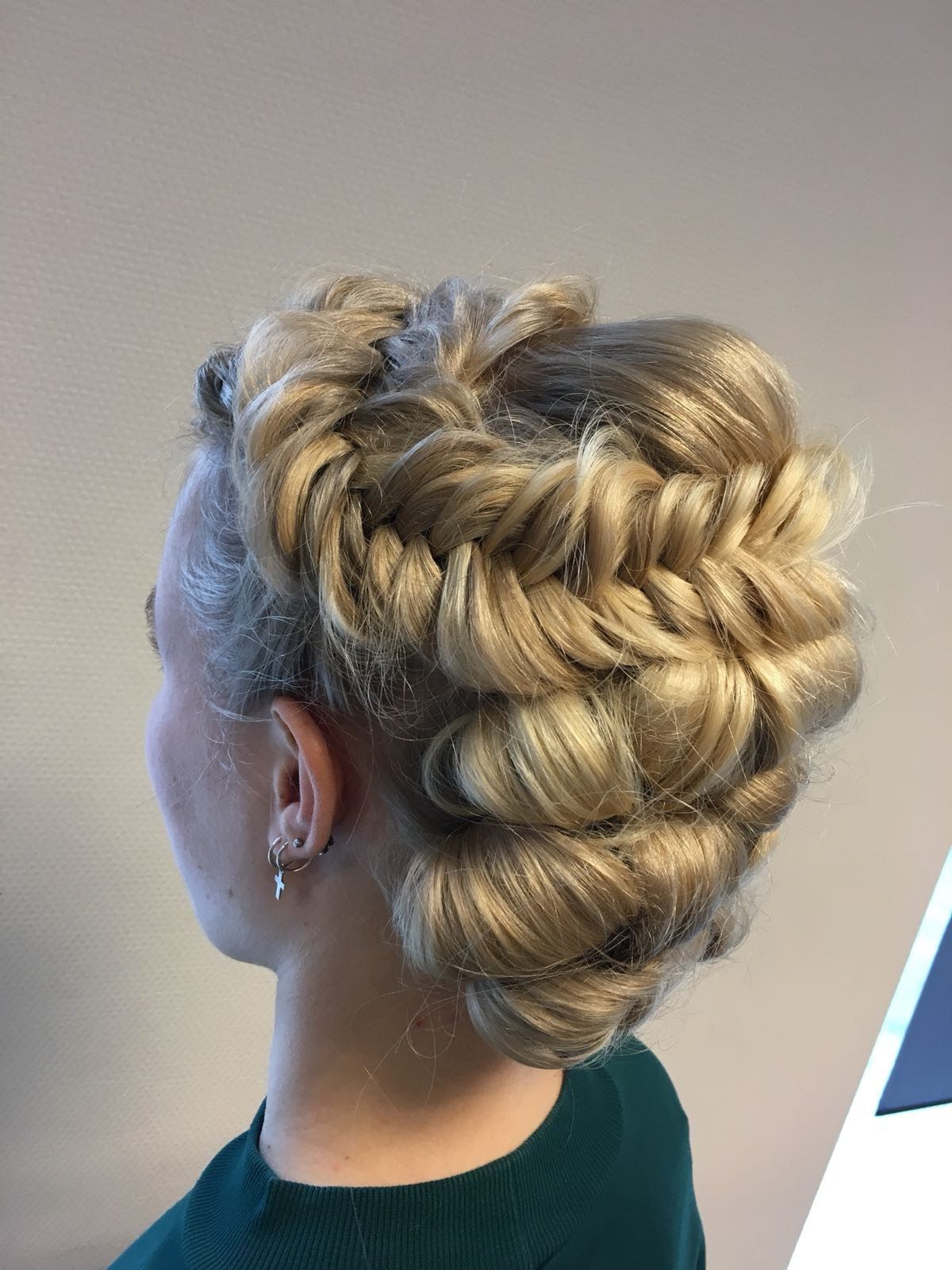 Ingewikkeld blond gevlochten opgestoken kapsel met gevlochten kroon, van de zijkant gezien tegen een effen achtergrond.