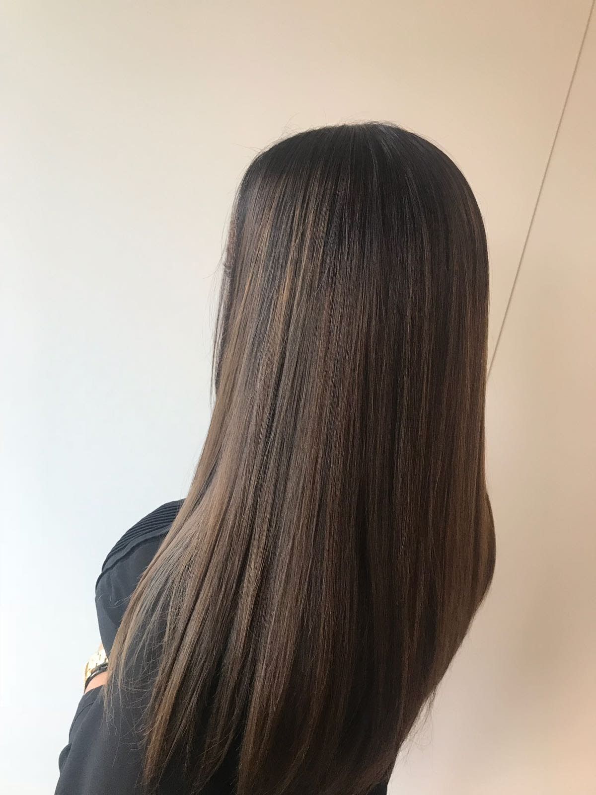 Lang, steil bruin haar, van achteren gezien tegen een effen beige muur.