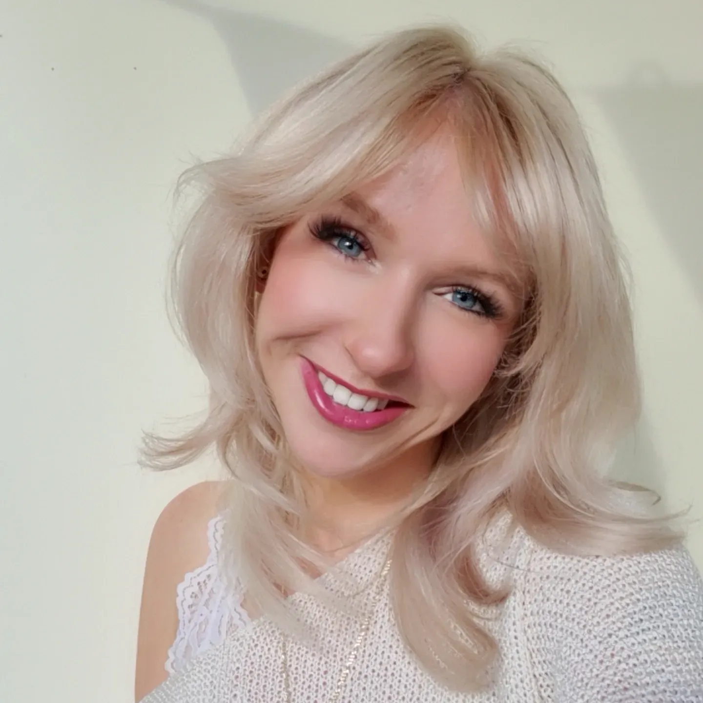 Lachende blonde vrouw in een witte kanten top tegen een zacht verlichte achtergrond.