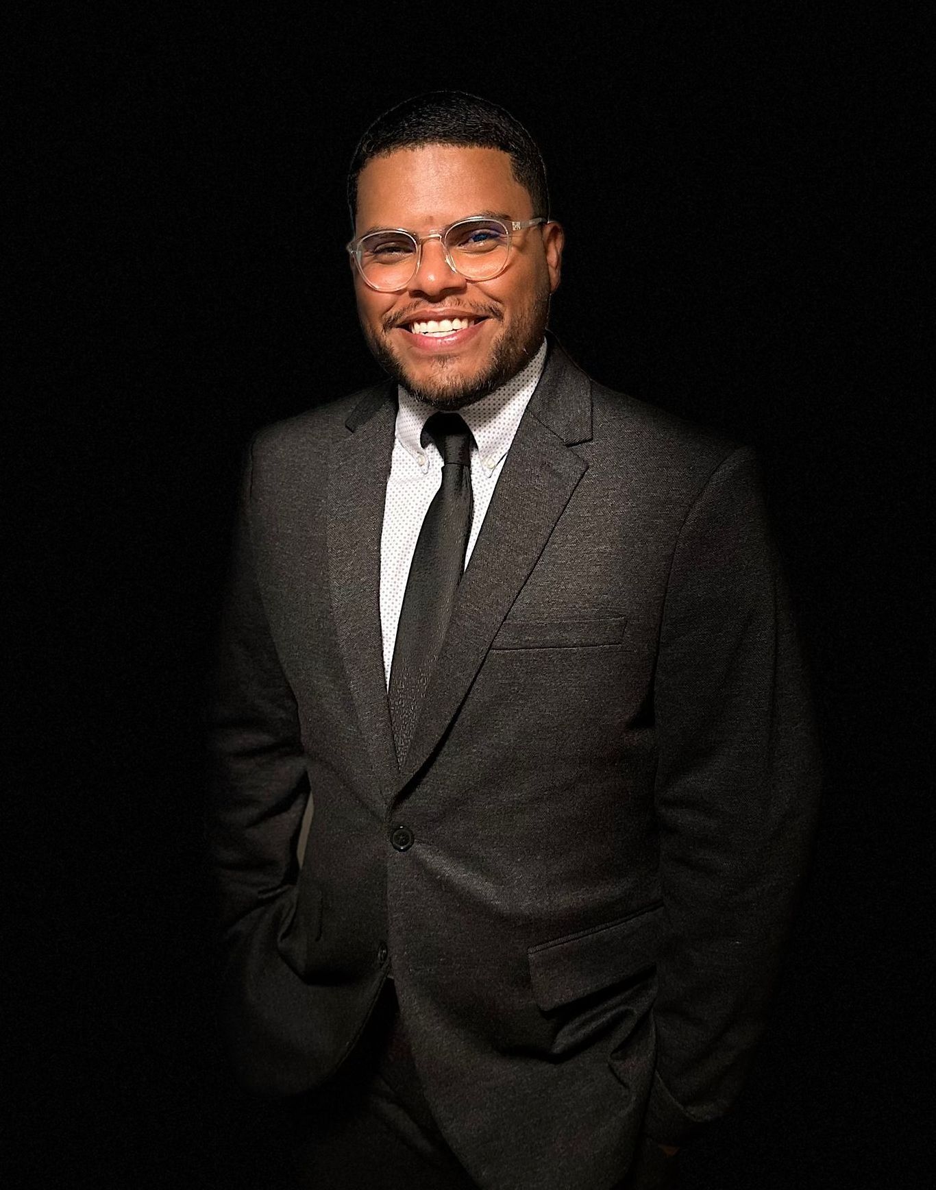 A man in a suit and tie is smiling in front of a black background.