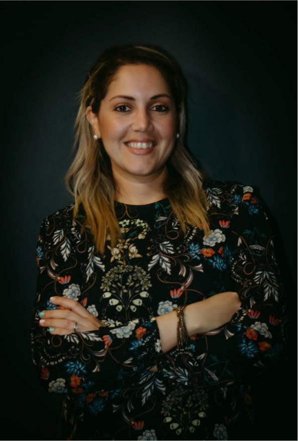 A woman in a floral shirt is smiling with her arms crossed.