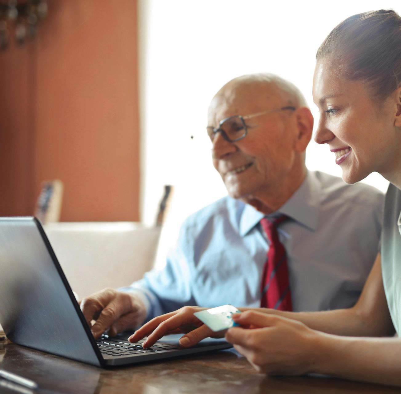 A man and a woman are sitting at a table looking at a laptop.