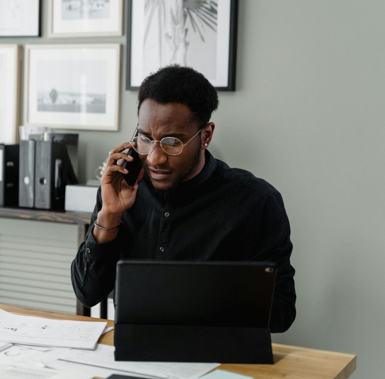 A man is sitting at a desk talking on a cell phone