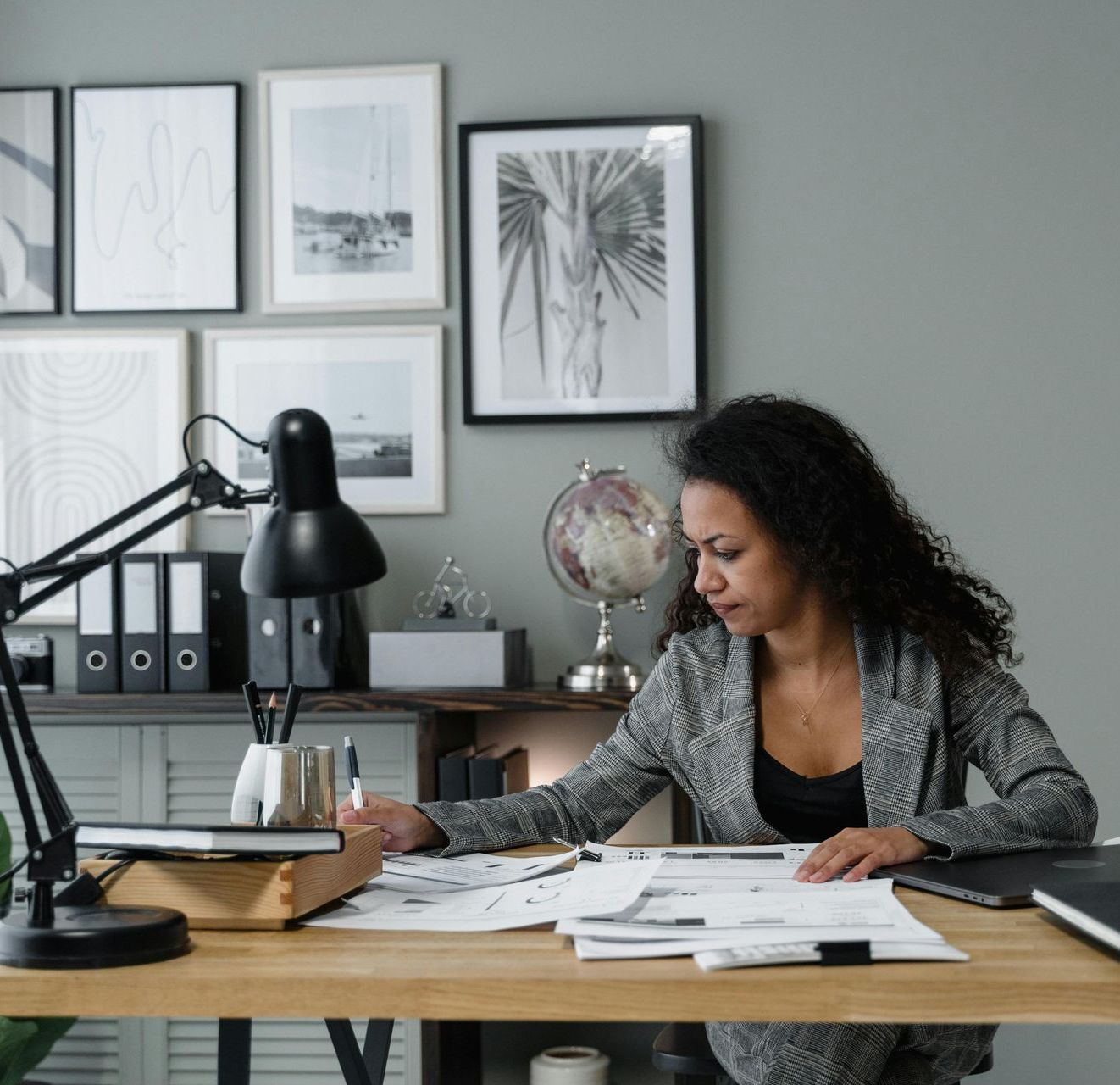 A woman is sitting at a desk with papers and a lamp.