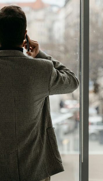 A man in a suit is talking on a cell phone while looking out of a window.