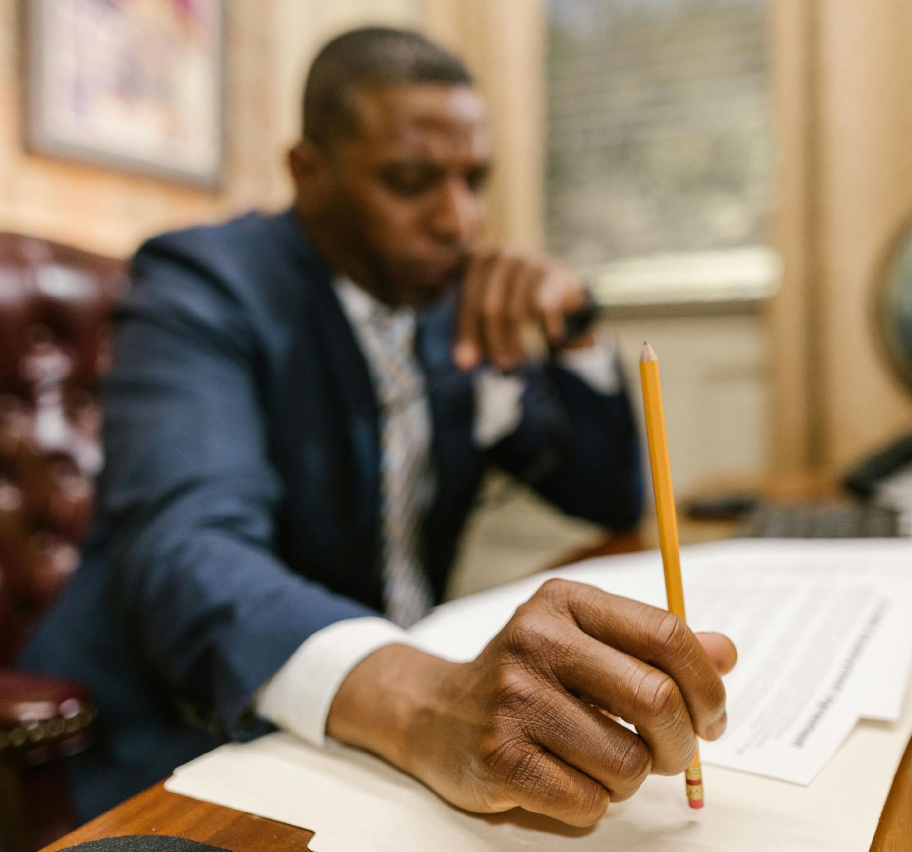 A man in a suit is writing on a piece of paper with a pencil