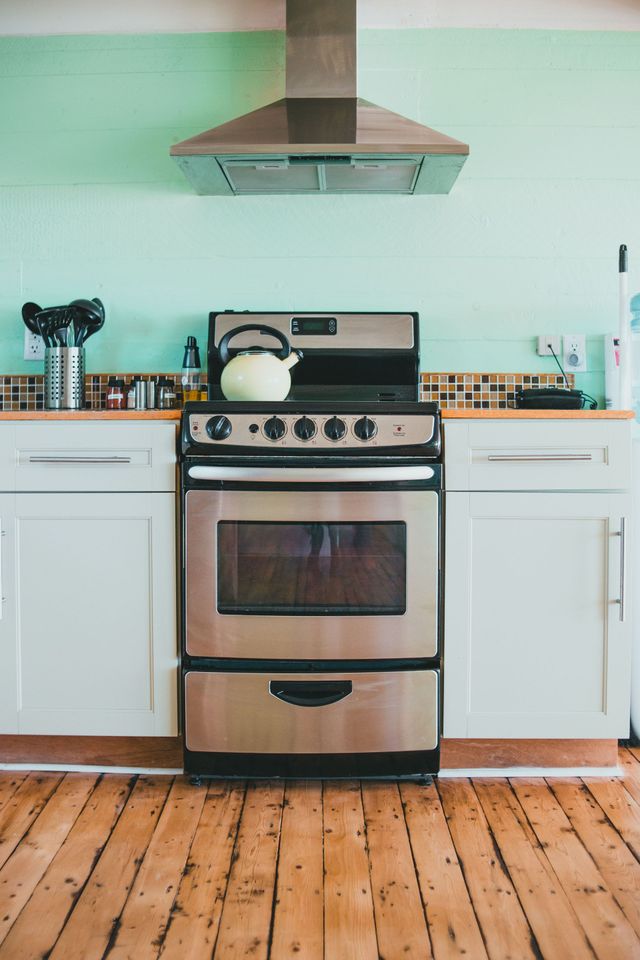 Stainless steel stove under a vent hood in a white kitchen with mint-green walls and wood floor
