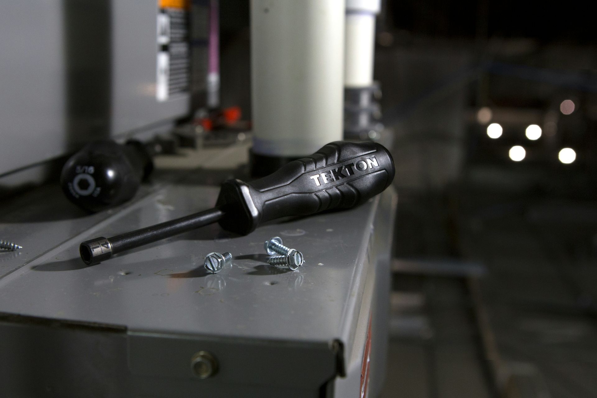 Screwdriver and scattered screws on a gray metal surface in an industrial setting