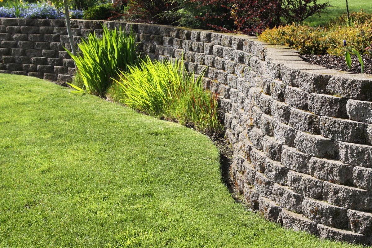 A stone wall surrounds a lush green lawn in a garden.