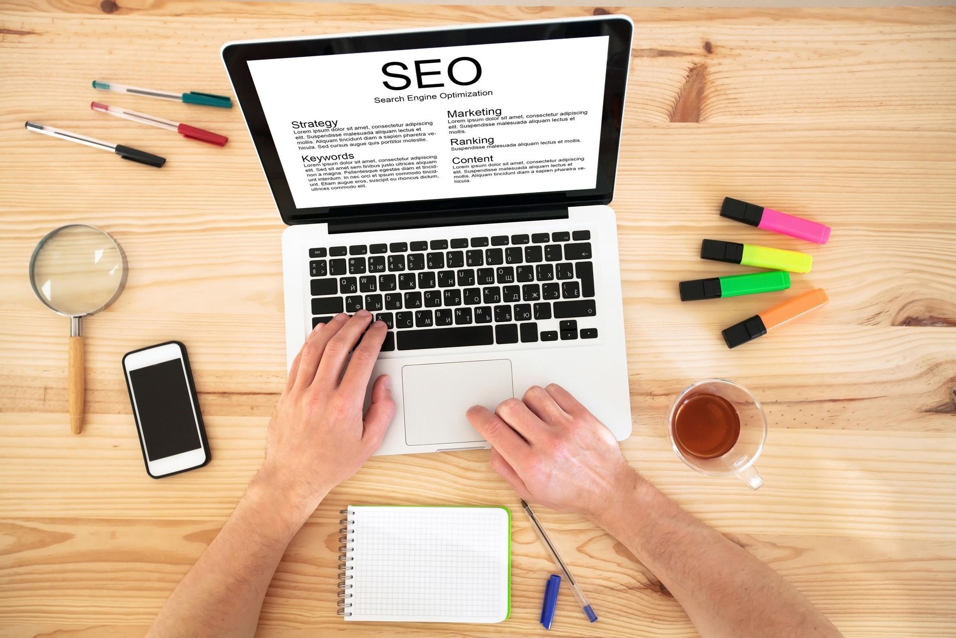 Hands typing on laptop with SEO webpage, surrounded by desk items and stationery