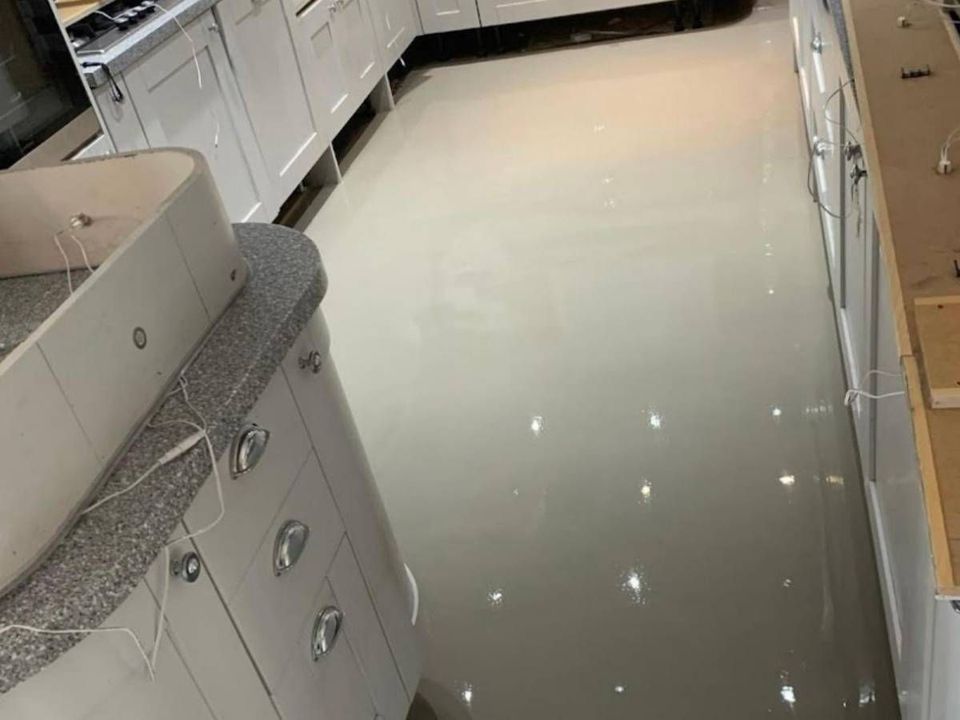 Freshly poured self-levelling screed across a kitchen floor between fitted units