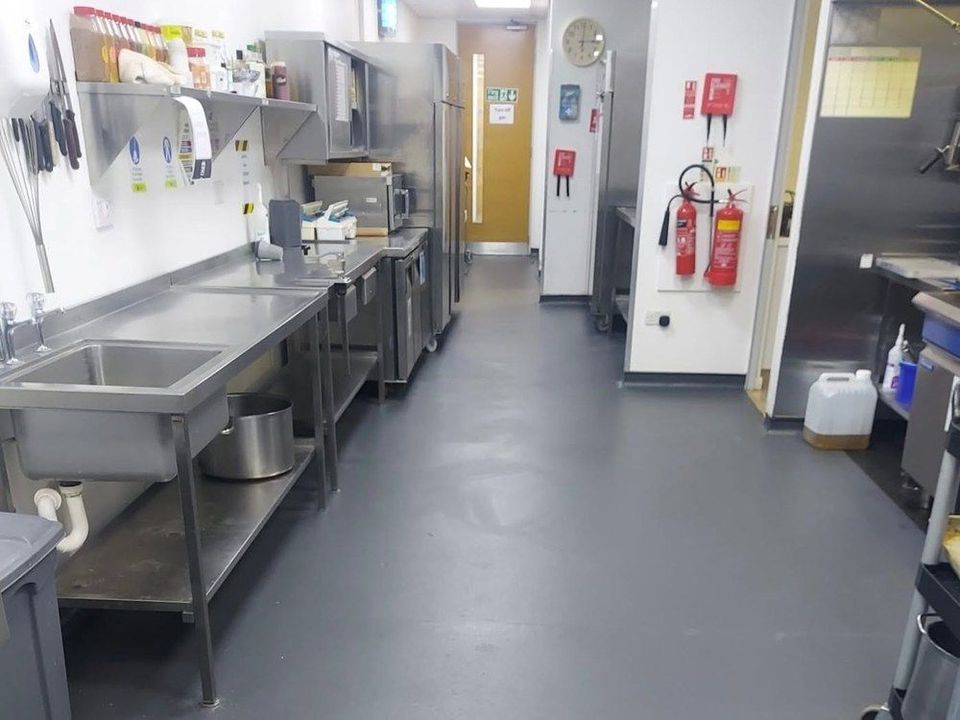 Grey safety vinyl flooring running through a commercial kitchen past stainless steel sinks and benches