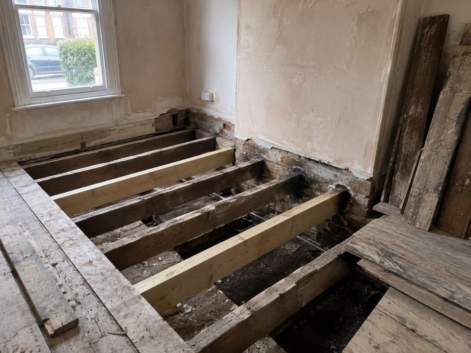 Floorboards lifted in an empty room to expose timber floor joists above the void