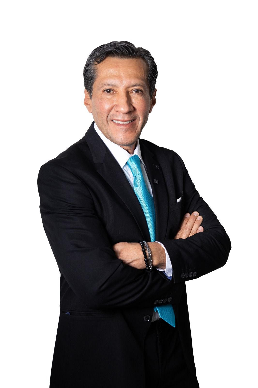 Hombre de traje negro con corbata turquesa y brazos cruzados, sonriendo.