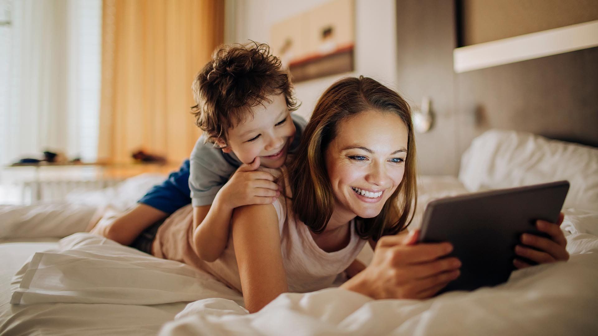 woman looks at tablet while a  young boy looks over her shoulder