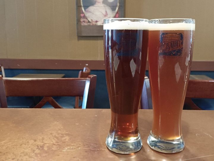 Two glasses of beer are sitting on a wooden table