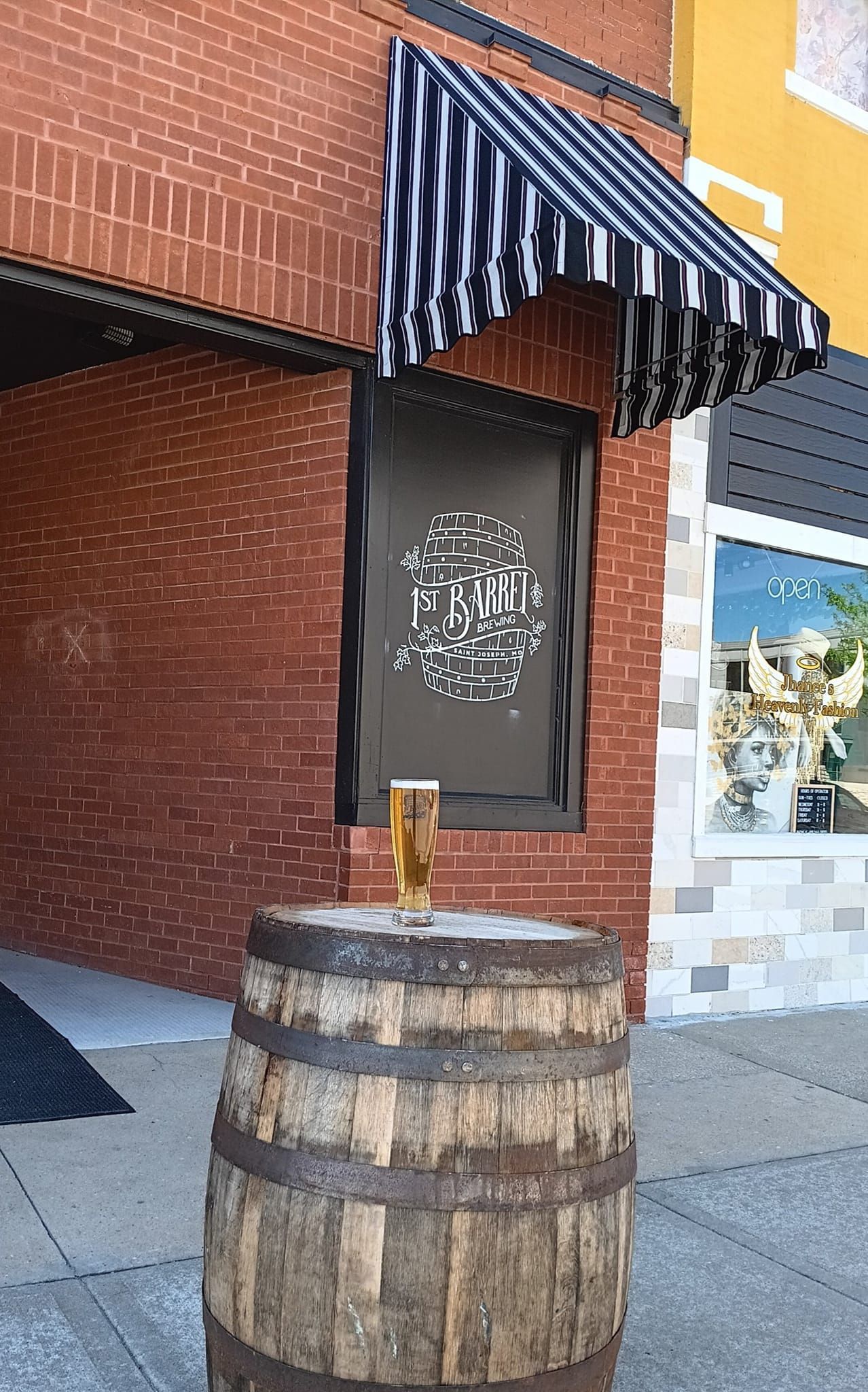 A wooden barrel is sitting in front of a brick building with a striped awning.