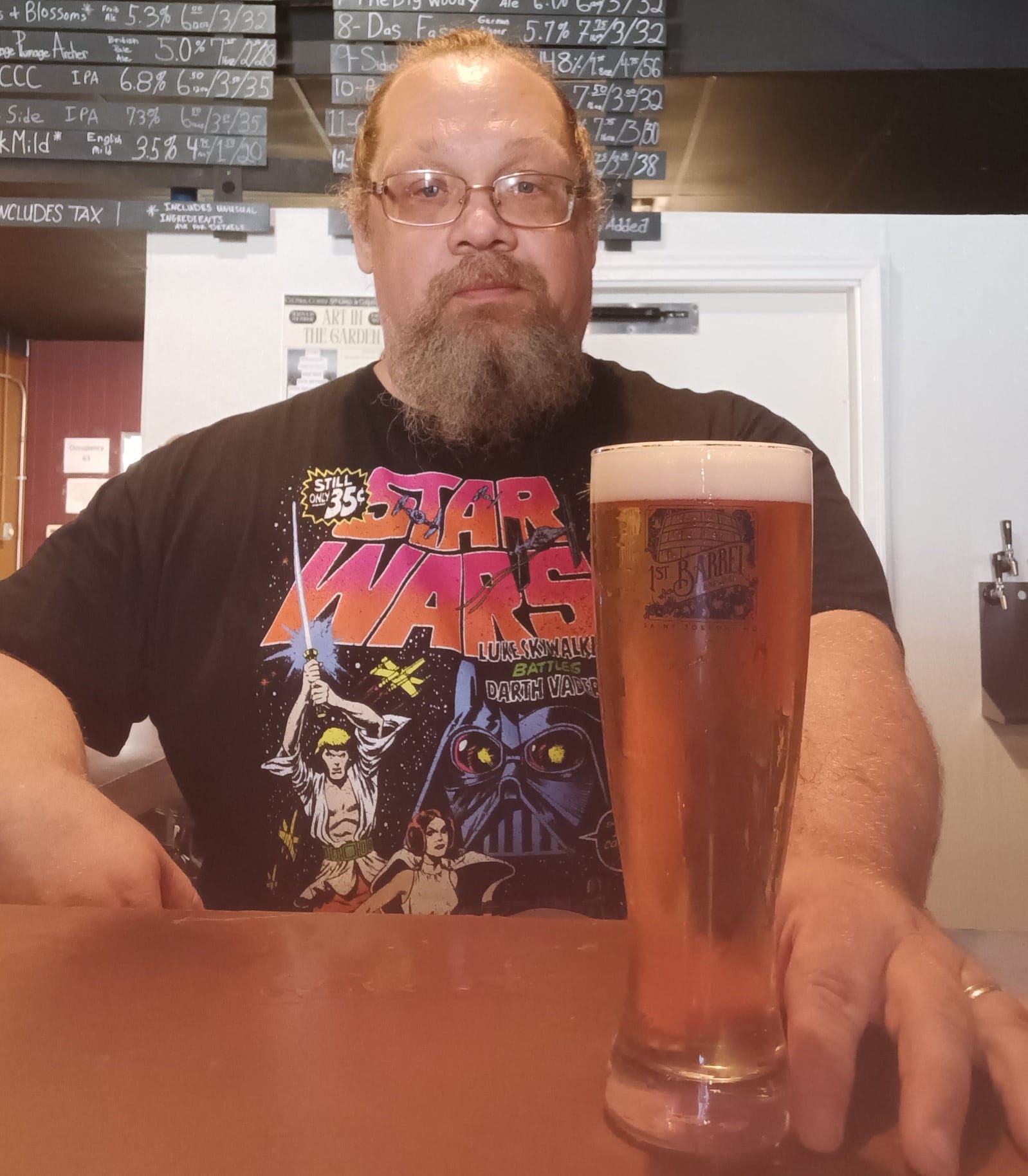 A man wearing a star wars shirt is holding a glass of beer