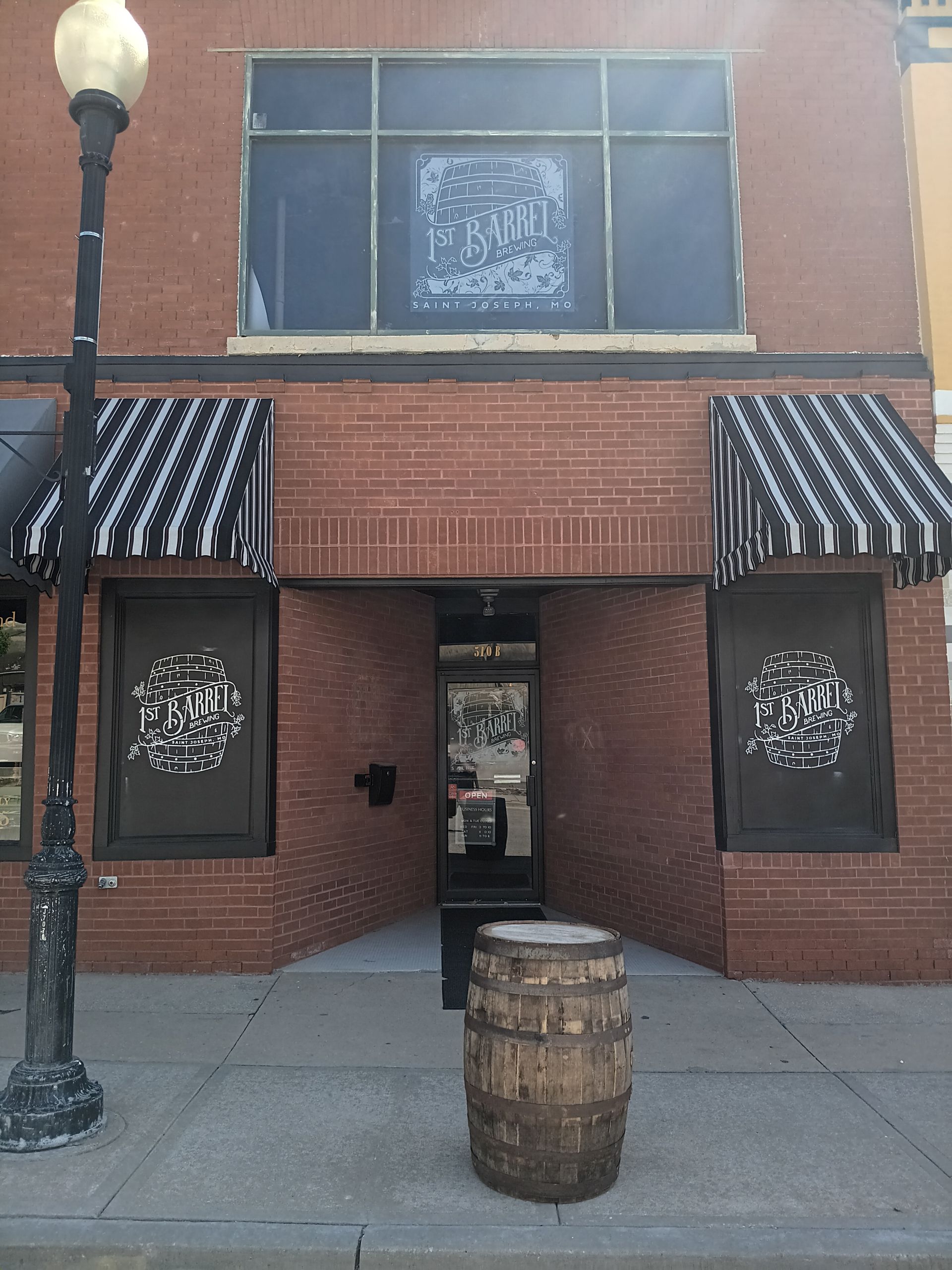 A brick building with black and white awnings and a barrel in front of it