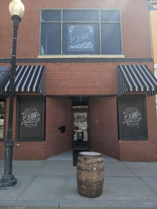 A brick building with black and white awnings and a barrel in front of it