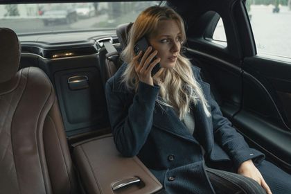 Woman in a dark coat talking on the phone in the back seat of a luxury car.