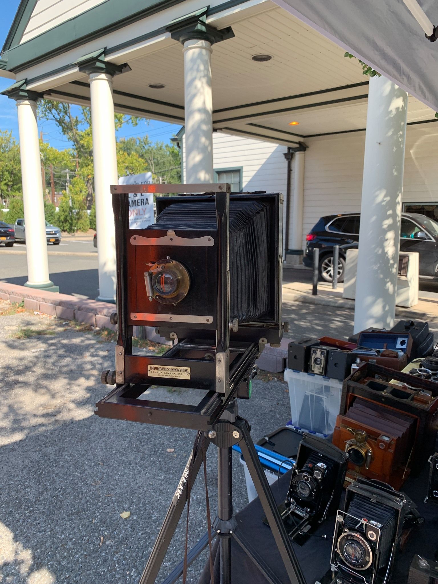 Vintage camera setup on a tripod beside antique equipment under a carport outdoors