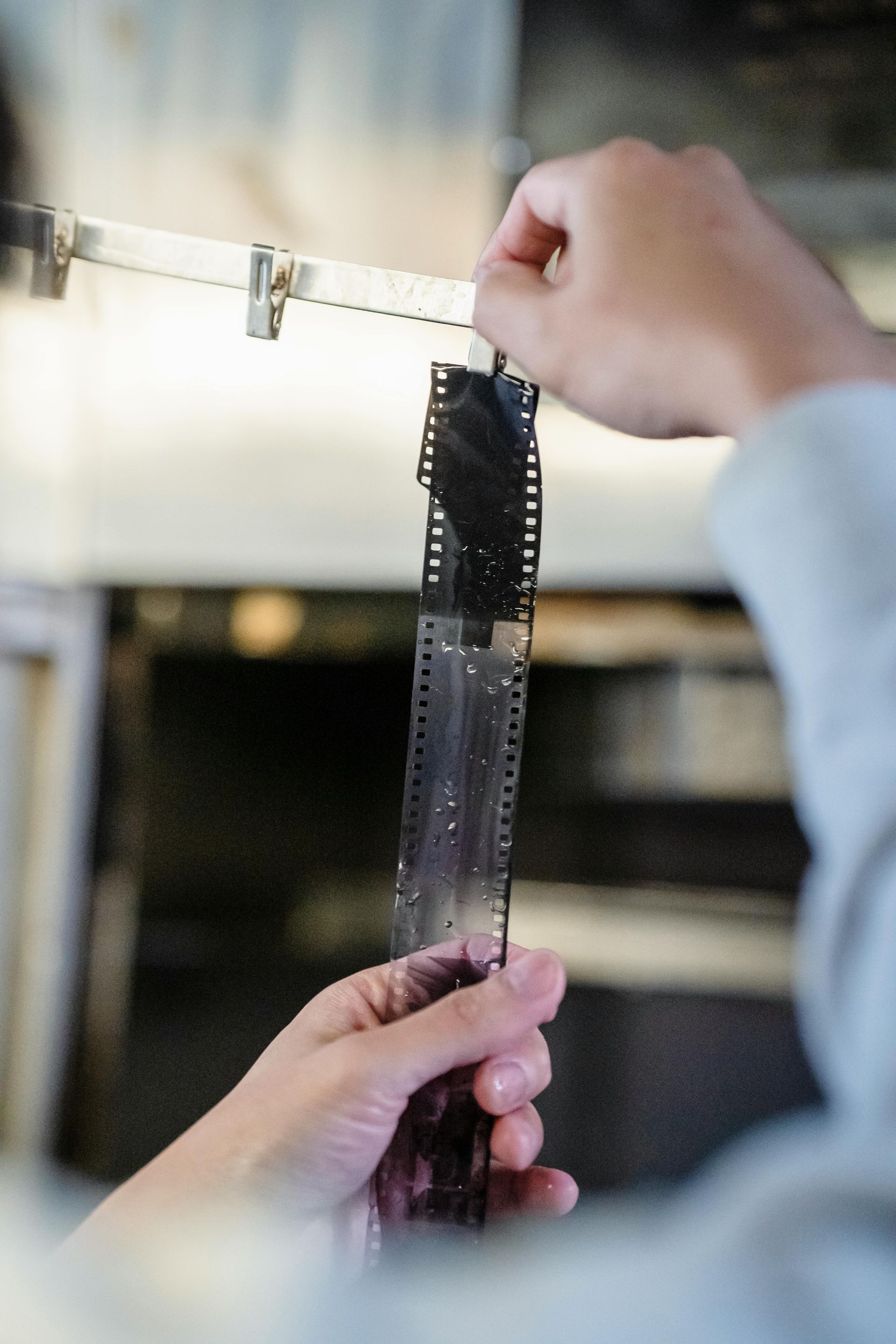 Hands hanging a long strip of black film negative against a bright background