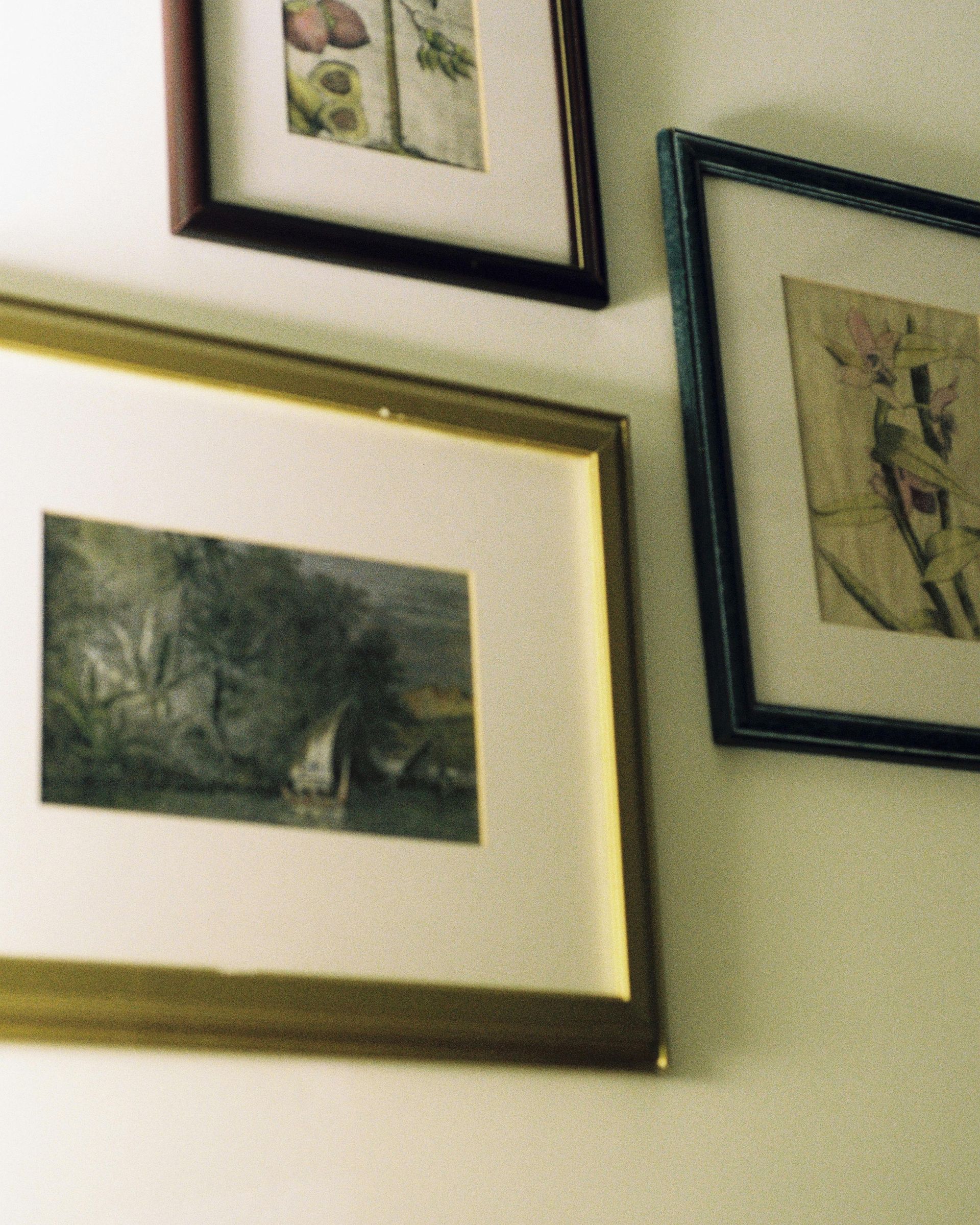 Three framed pictures hanging on a pale green wall, including a large gold-framed landscape.