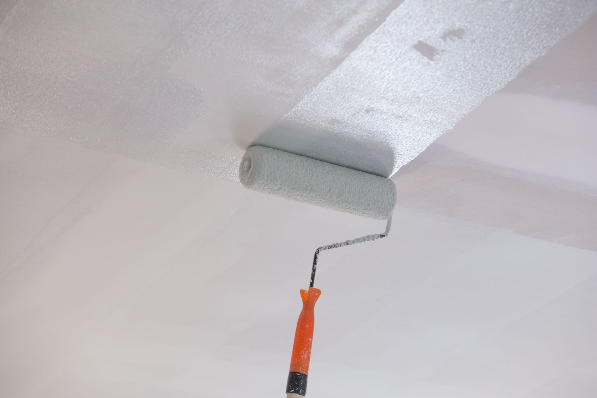 A paint roller applies a layer of white paint to a ceiling surface. A paint roller applies a layer of white paint to a ceiling surface.