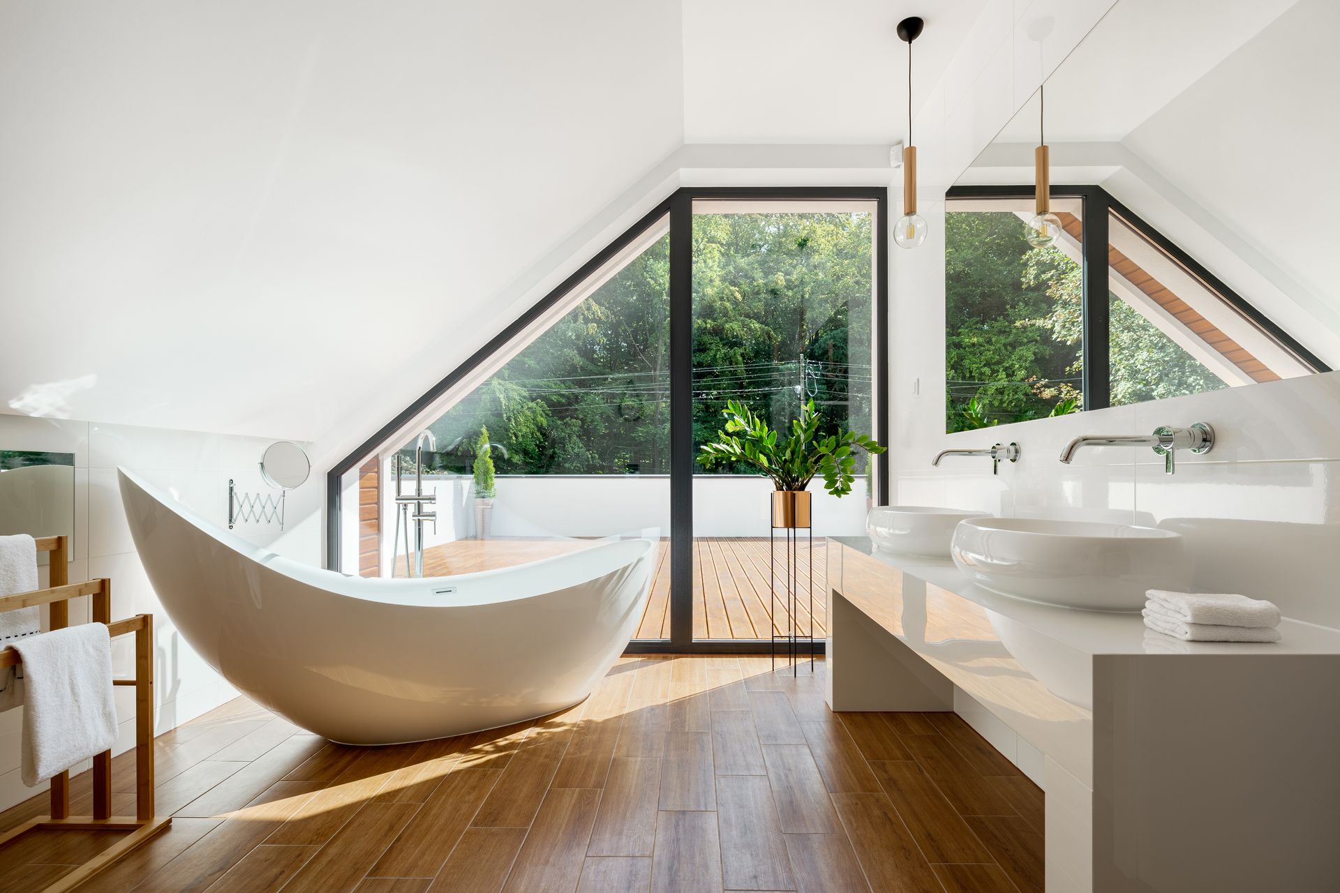 A modern, white bathroom with a curved freestanding tub, wood flooring, and a large window looking onto a green deck. A modern, white bathroom with a curved freestanding tub, wood flooring, and a large window looking onto a green deck.