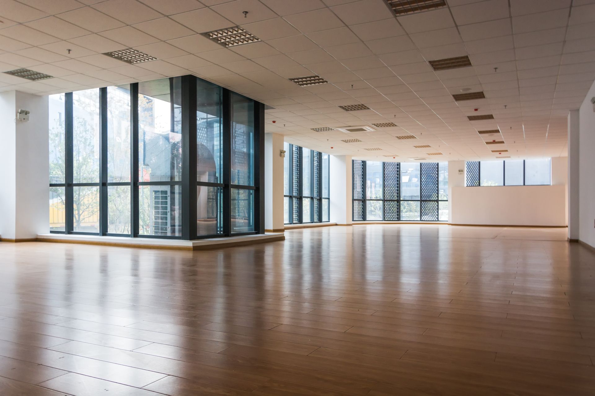A bright, empty open-plan office with polished wood floors, high ceilings, and floor-to-ceiling windows. A bright, empty open-plan office with polished wood floors, high ceilings, and floor-to-ceiling windows.