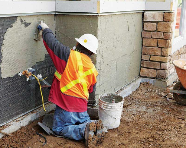 “Worker in safety gear applying fresh stucco coating to the base of a home exterior during a stucco service in Henderson, NV”