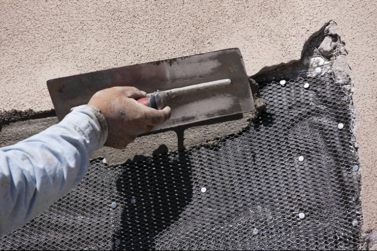 “Close-up of a trowel spreading dark stucco material across a textured exterior wall during a stucco service in Henderson, NV”