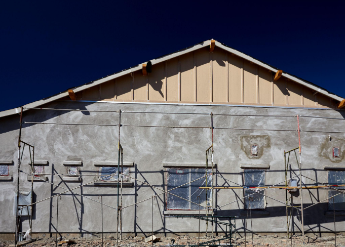 “Residential exterior covered in fresh gray stucco with scaffolding along the wall during a stucco service in Henderson, NV”